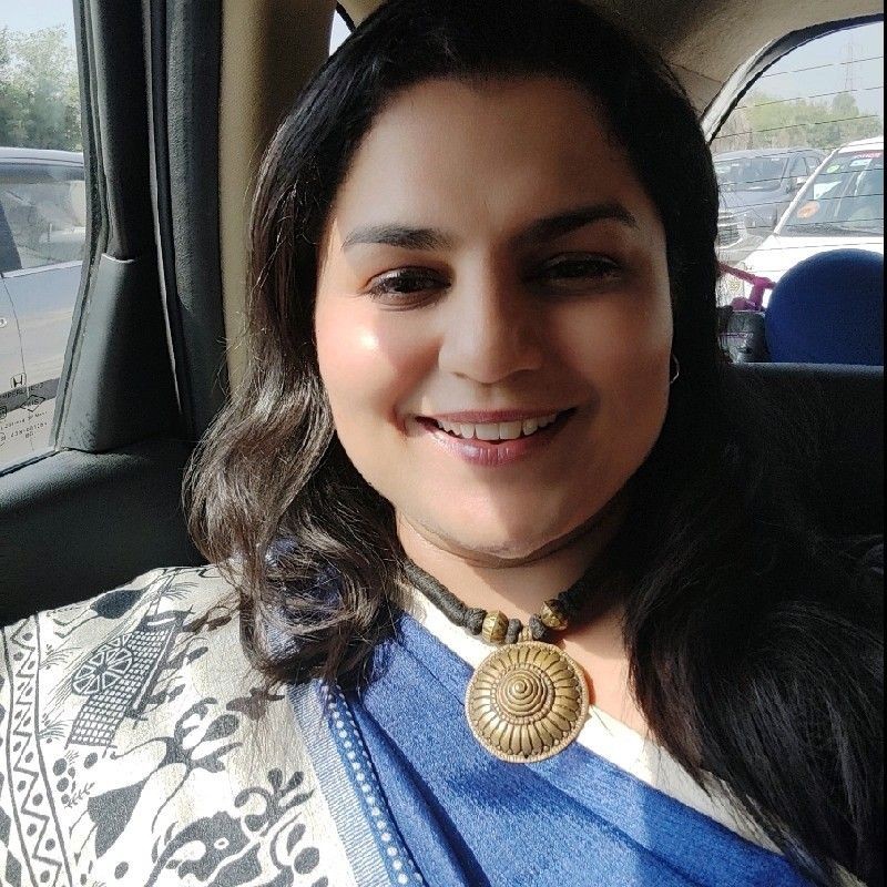 Smiling person in a car wearing a blue and white patterned outfit with a large circular necklace.